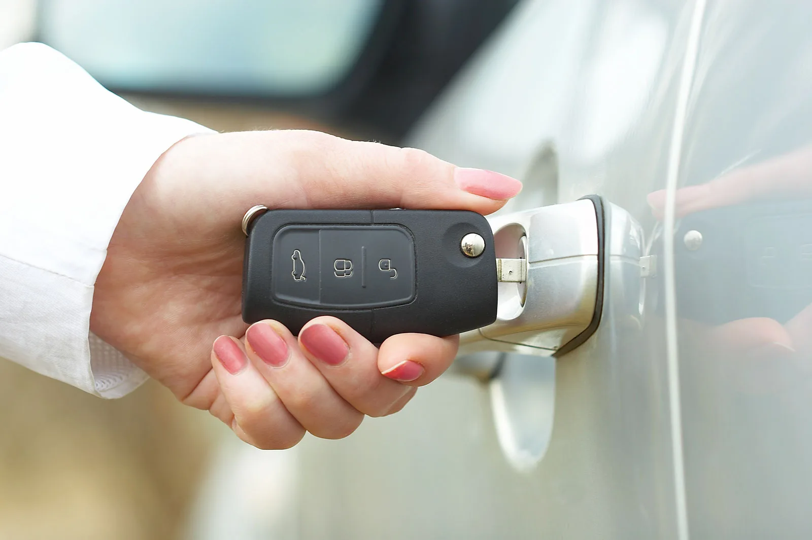 Hand holding a car key fob beside a vehicle door